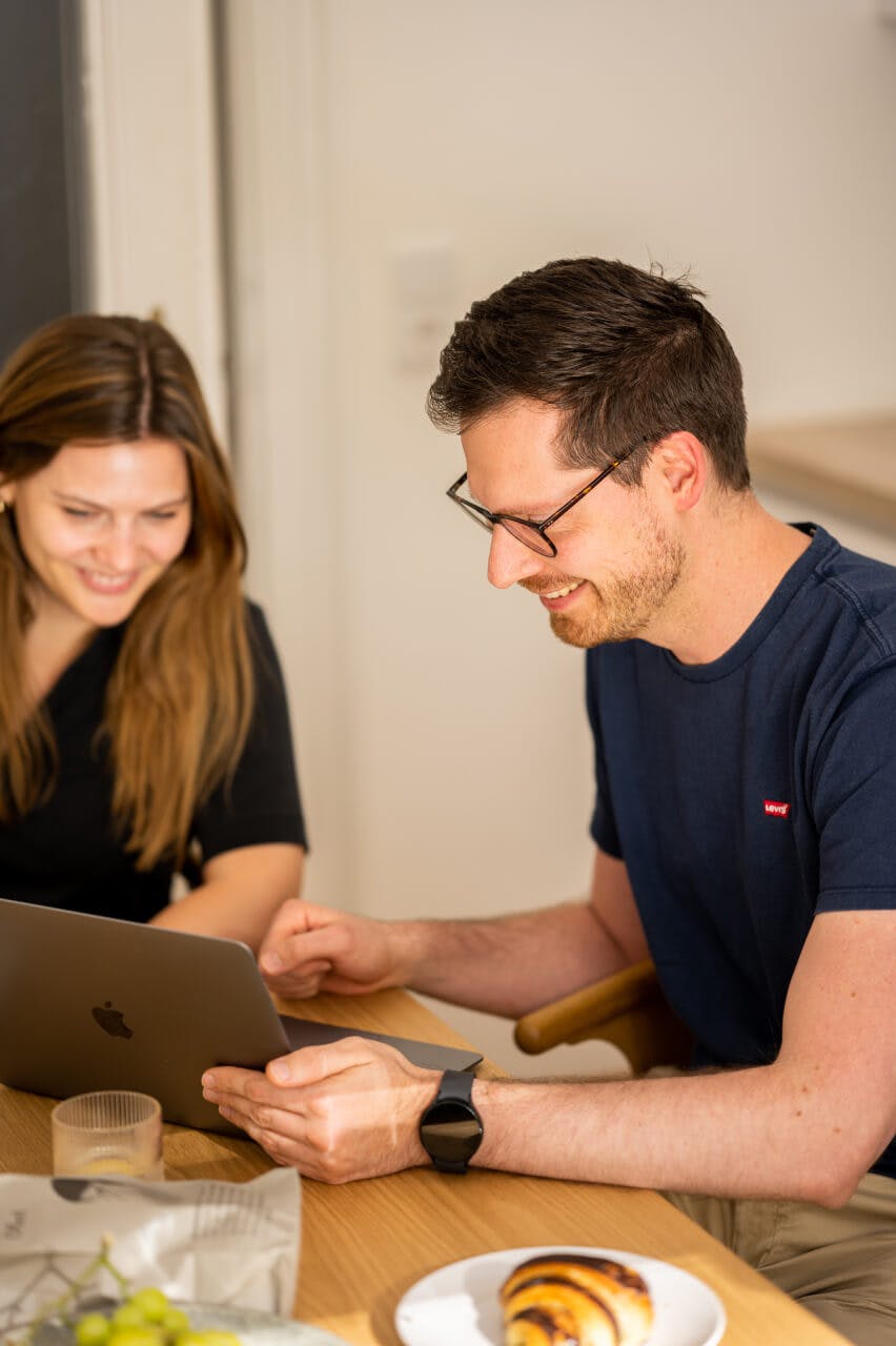 Zwei Personen arbeiten in ungezwungener Atmosphäre an einem Laptop in einer Digitalagentur in Wien zusammen.